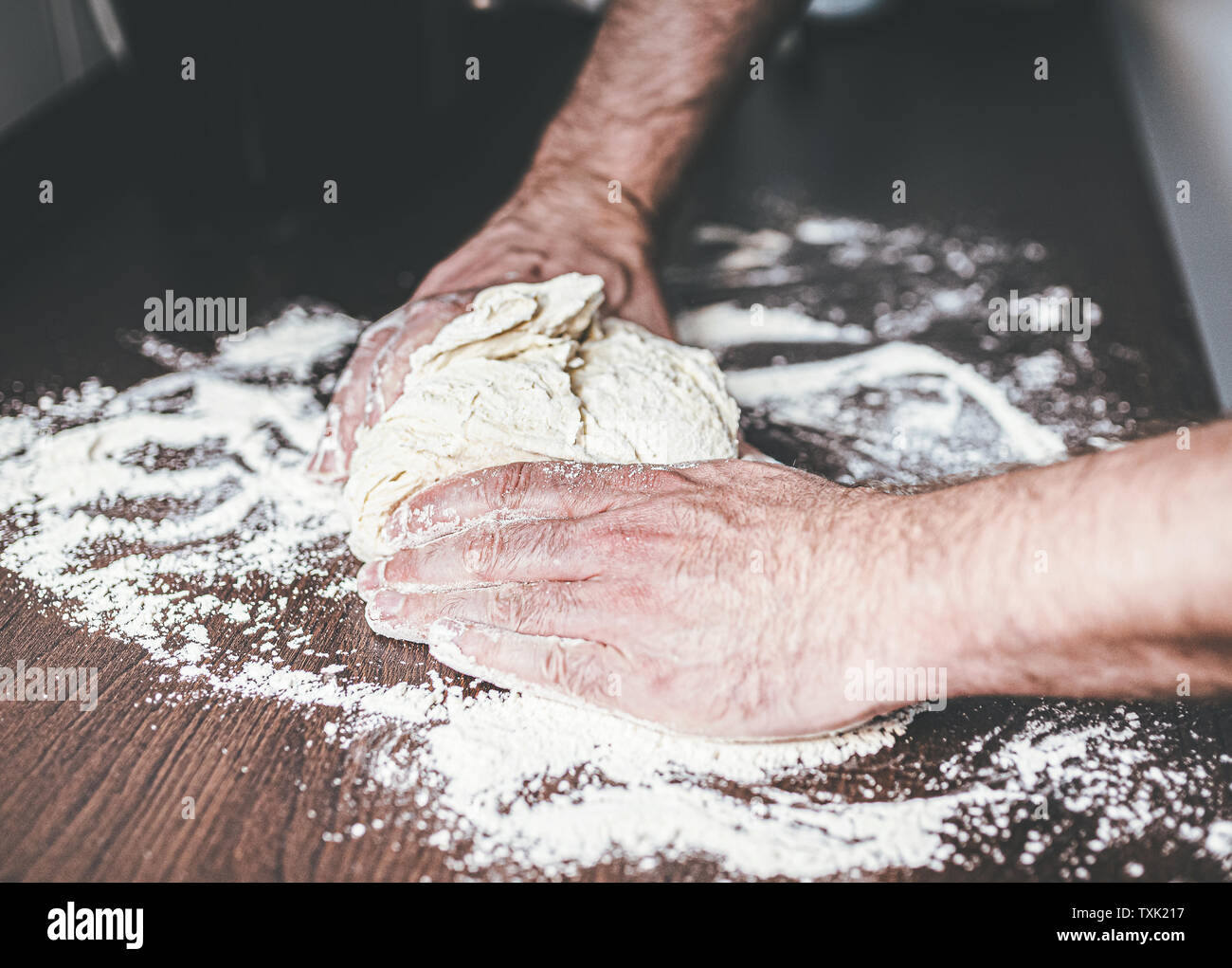 Gros plan des mains de l'homme du pétrissage de la pâte sur le plan de travail fariné Banque D'Images