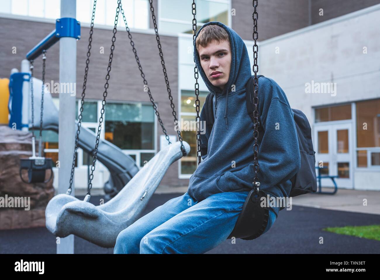 Triste adolescent assis sur une balançoire à l'extérieur de l'école. Il est des souvenirs de quand il était jeune. Banque D'Images