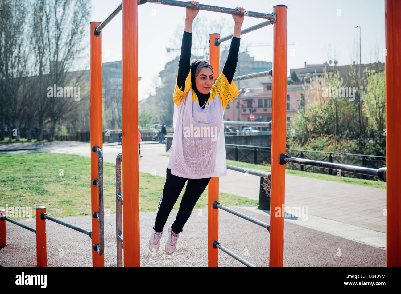 La classe de gymnastique suédoise au sport en plein air, jeune femme se balançant d'équipement d'exercice Banque D'Images