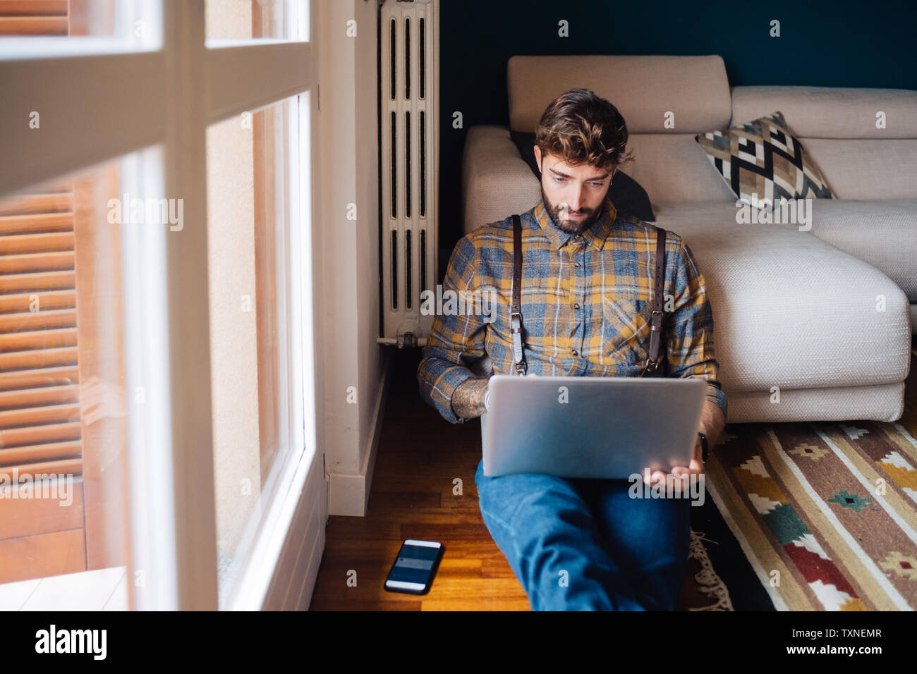 Mid adult man sitting on plancher du salon looking at laptop Banque D'Images