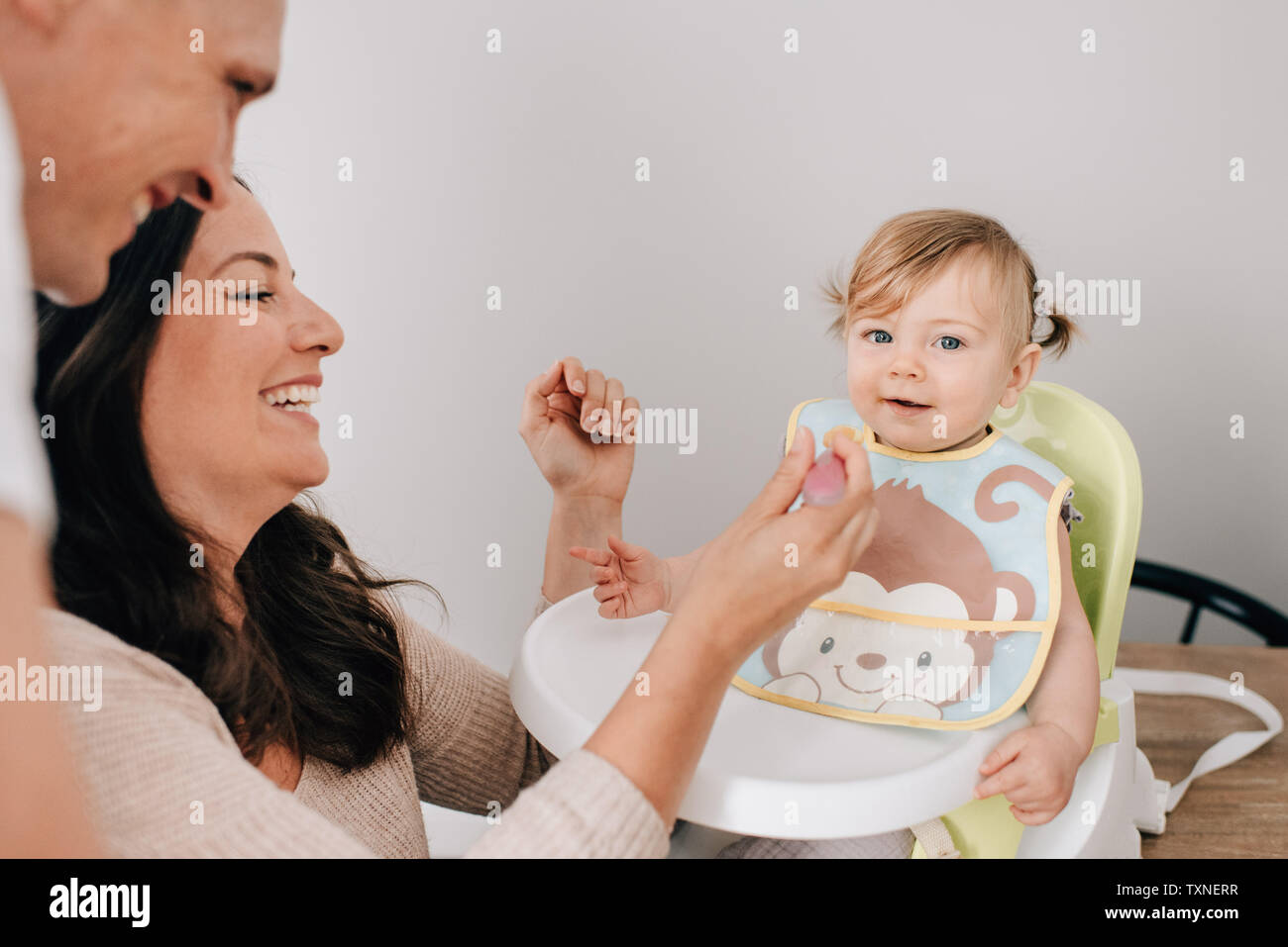 Mère et père nourrir bébé fille dans un siège pour enfant, portrait Banque D'Images