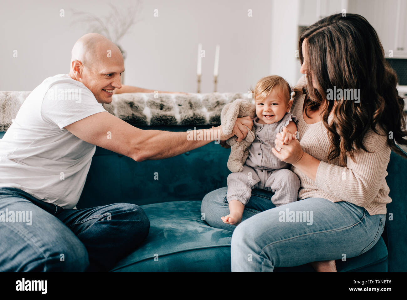 Mère et père sur canapé avec bébé fille jouer avec doudou Banque D'Images