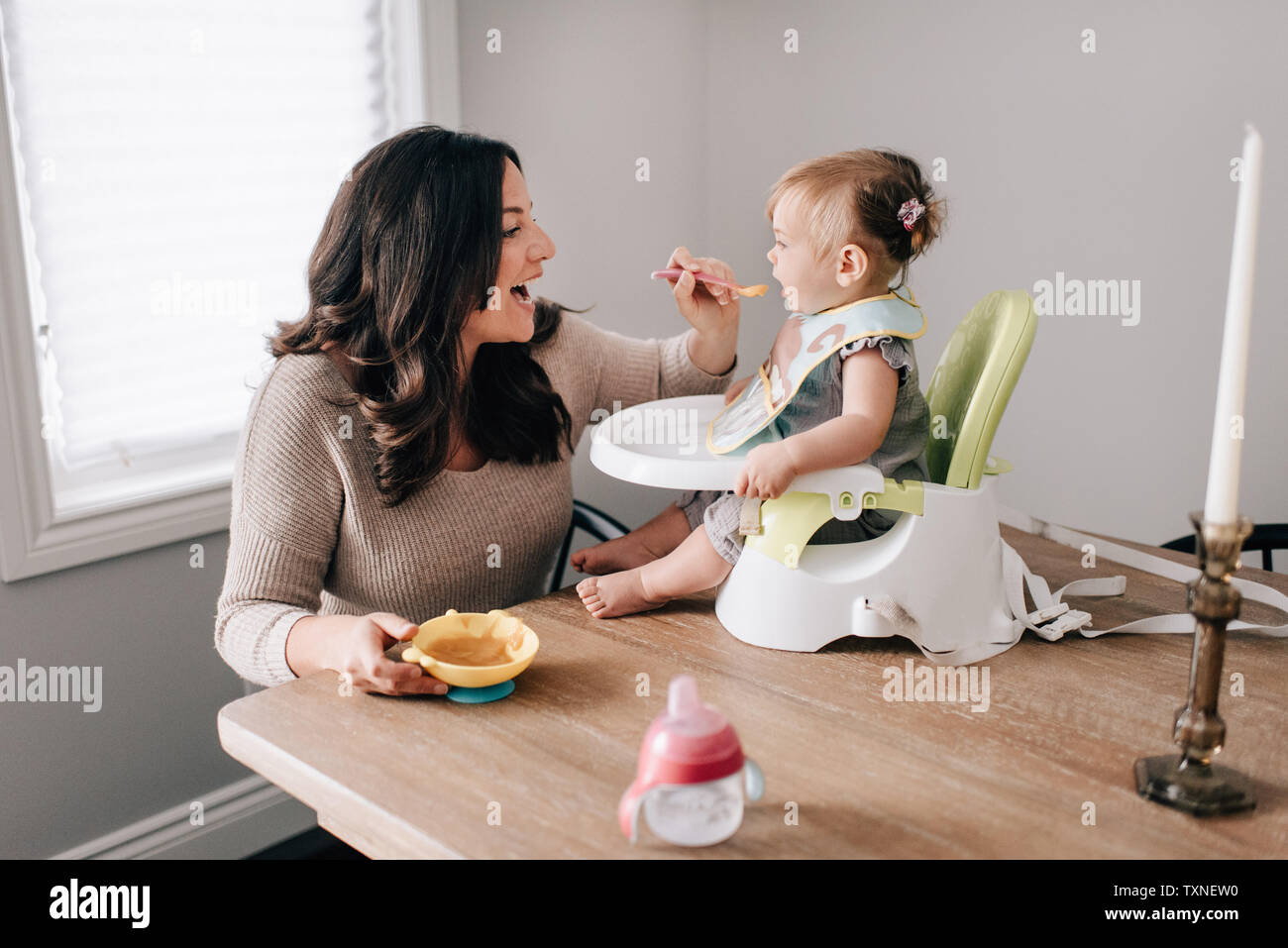 Mère nourrir bébé fille en siège enfant sur table de cuisine Banque D'Images
