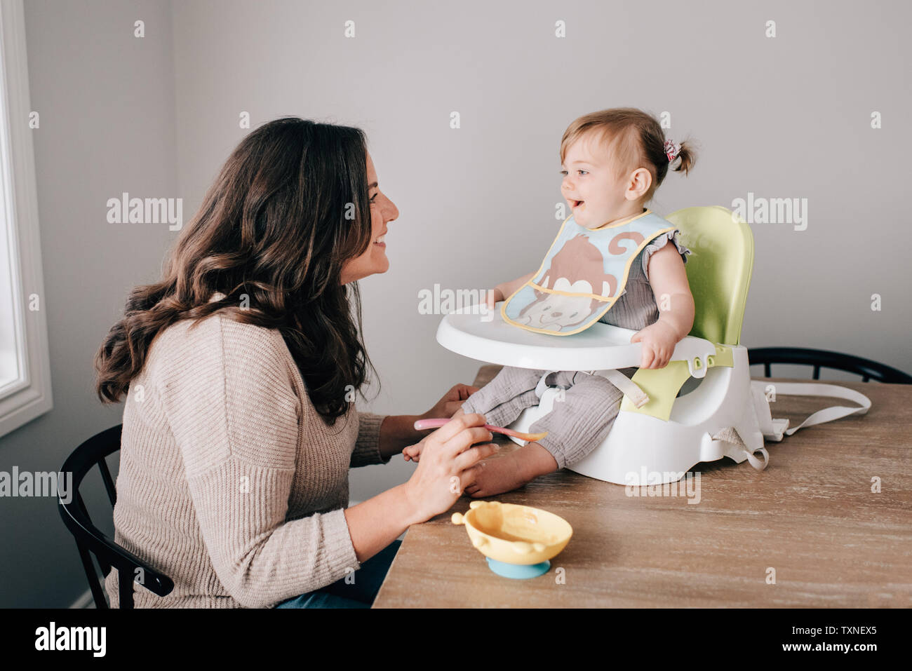 Mère nourrir bébé fille en siège enfant sur table de cuisine Banque D'Images