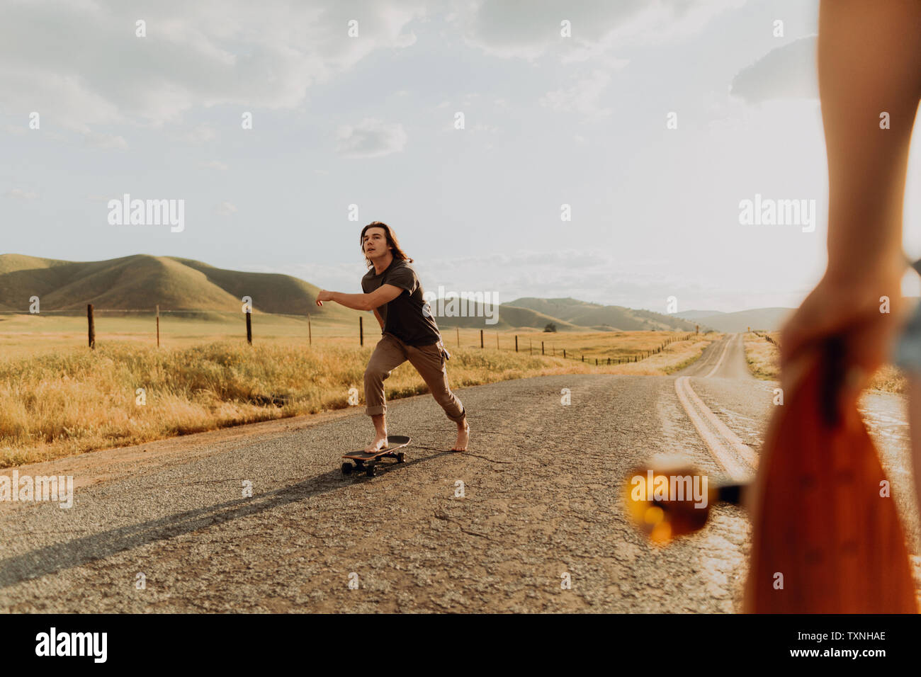 Les jeunes hommes nus skate skateboarder on rural road, petite amie observant, Exeter, California, USA Banque D'Images