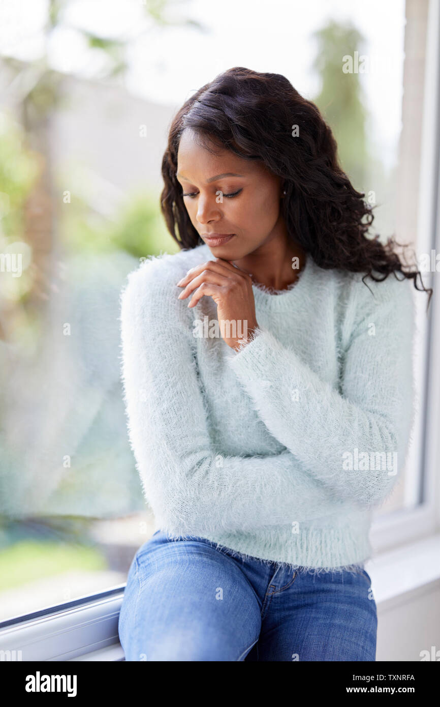 Femme ethnique à la triste assis dans une fenêtre Banque D'Images