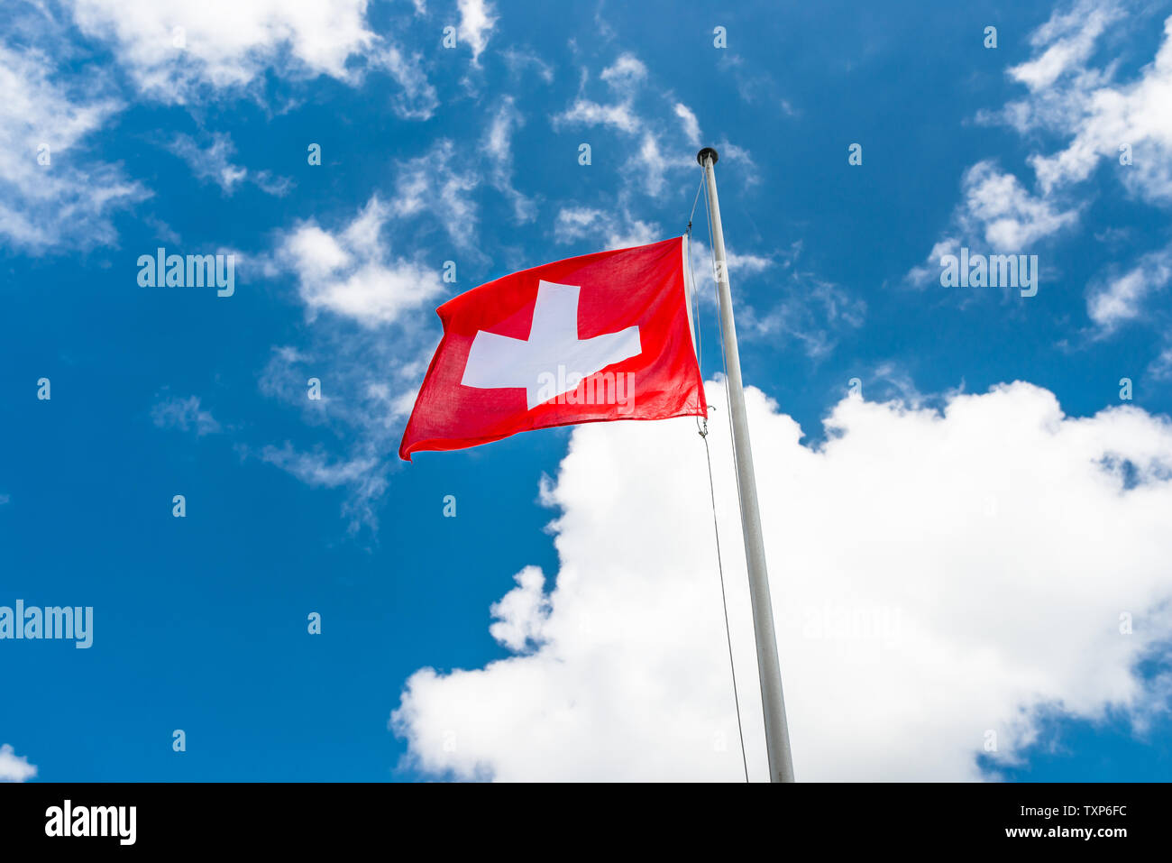 Dans le vent à gauche, le drapeau de la Suisse accrochée au mât, sur le fond bleu du ciel avec des nuages blancs. Banque D'Images