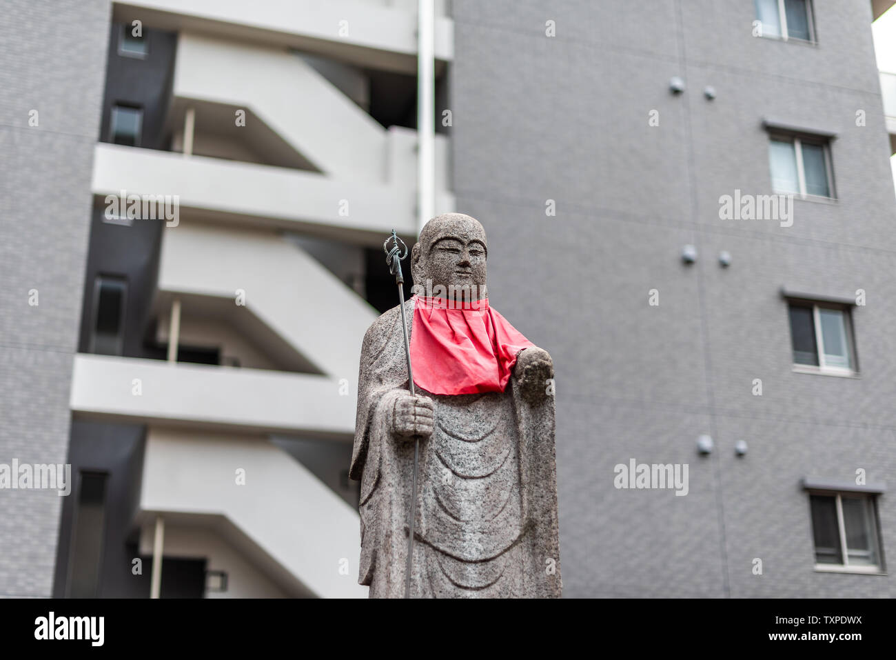 Osaka, Japon statue Jizo avec dossard rouge isolé sur fond d'immeuble moderne au centre-ville de ville Banque D'Images