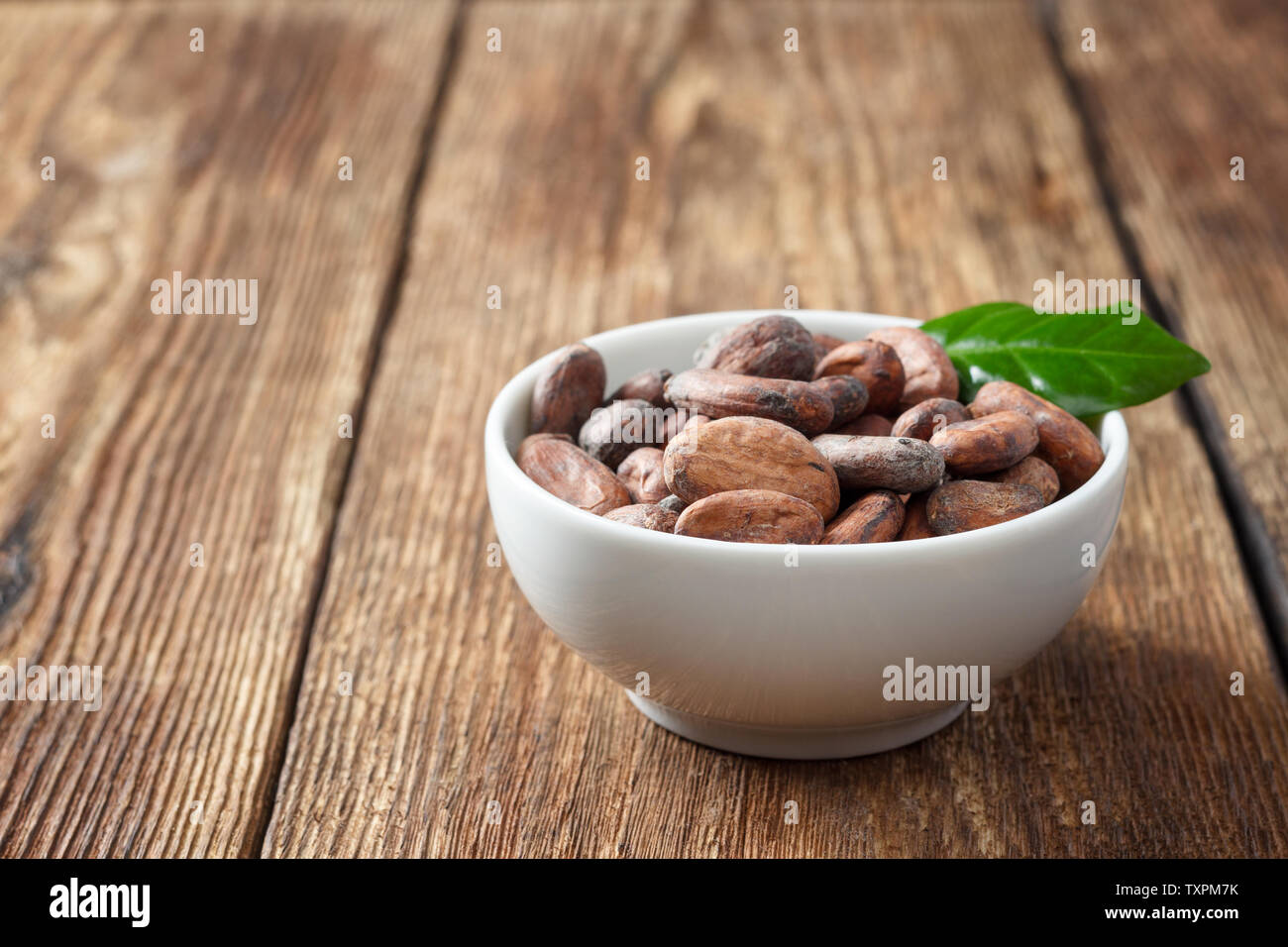 Les fèves de cacao dans un bol blanc sur une table en bois Photo Stock -  Alamy