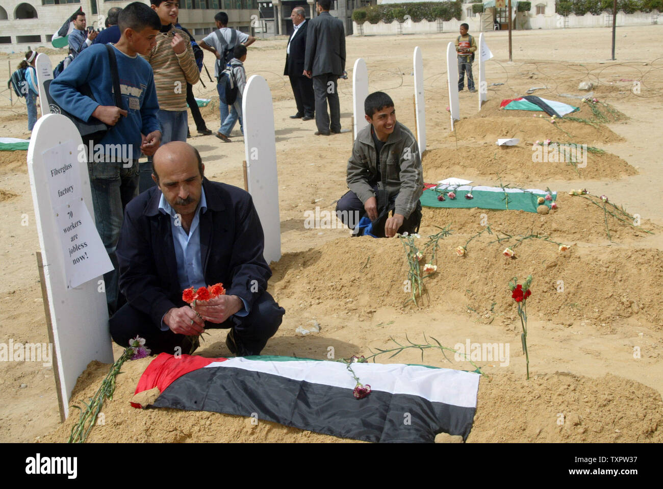 Les hommes palestiniens mettre des fleurs sur les tombes au cimetière une maquette créé pour symboliser la mort de l'économie en raison du blocus israélien de Gaza le 18 mars 2008. Une association palestinienne installé la maquette des tombes dans un espace public dans la ville meurtrie par la guerre pour représenter la mort de Gaza par les entreprises. Le taux de chômage dans le territoire 70  %, des entreprises privées à travers la bande de Gaza se sont effondrés, et de l'eau et pénuries d'électricité ont sapé le secteur de la santé local. (Photo d'UPI/Ismael Mohamad) Banque D'Images