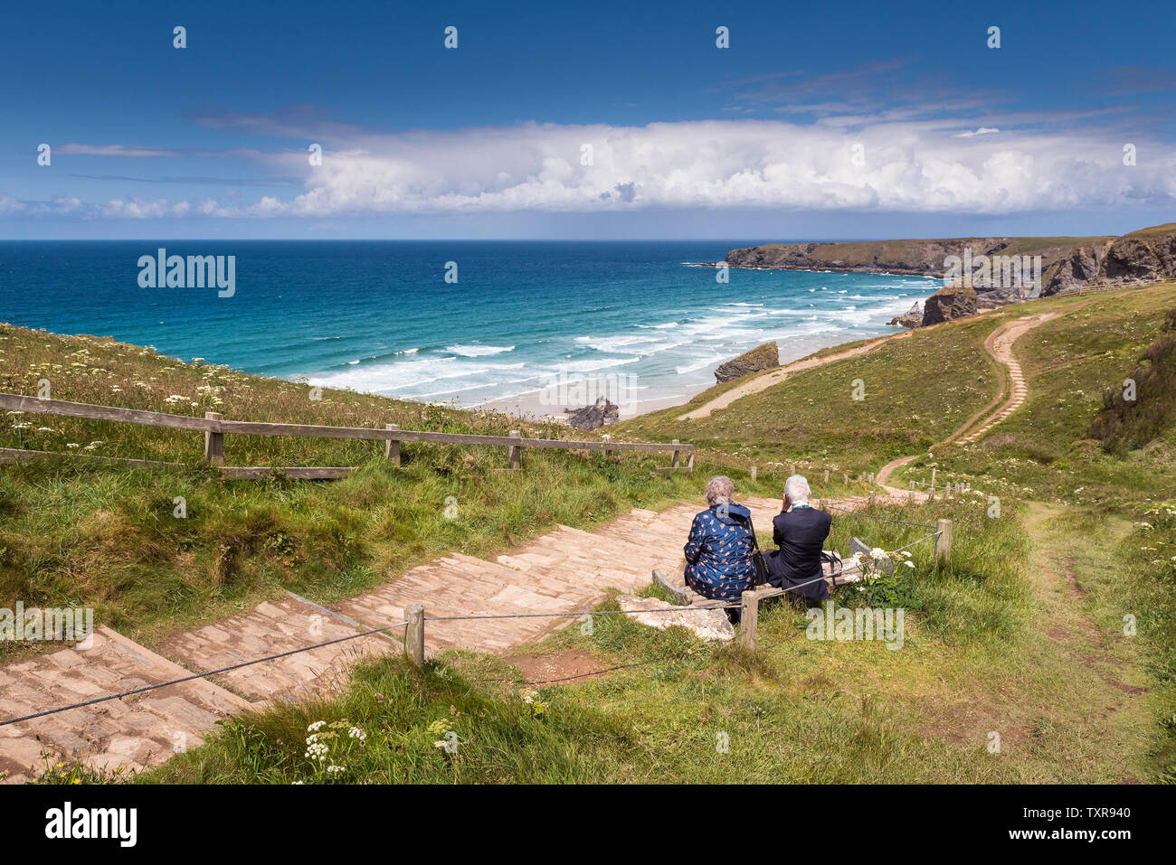Un jeune couple assis sur un banc et profiter de la vue sur la côte spectaculaire, robuste à Carnewas et Bedruthan Steps sur la Cornouailles du Nord Banque D'Images