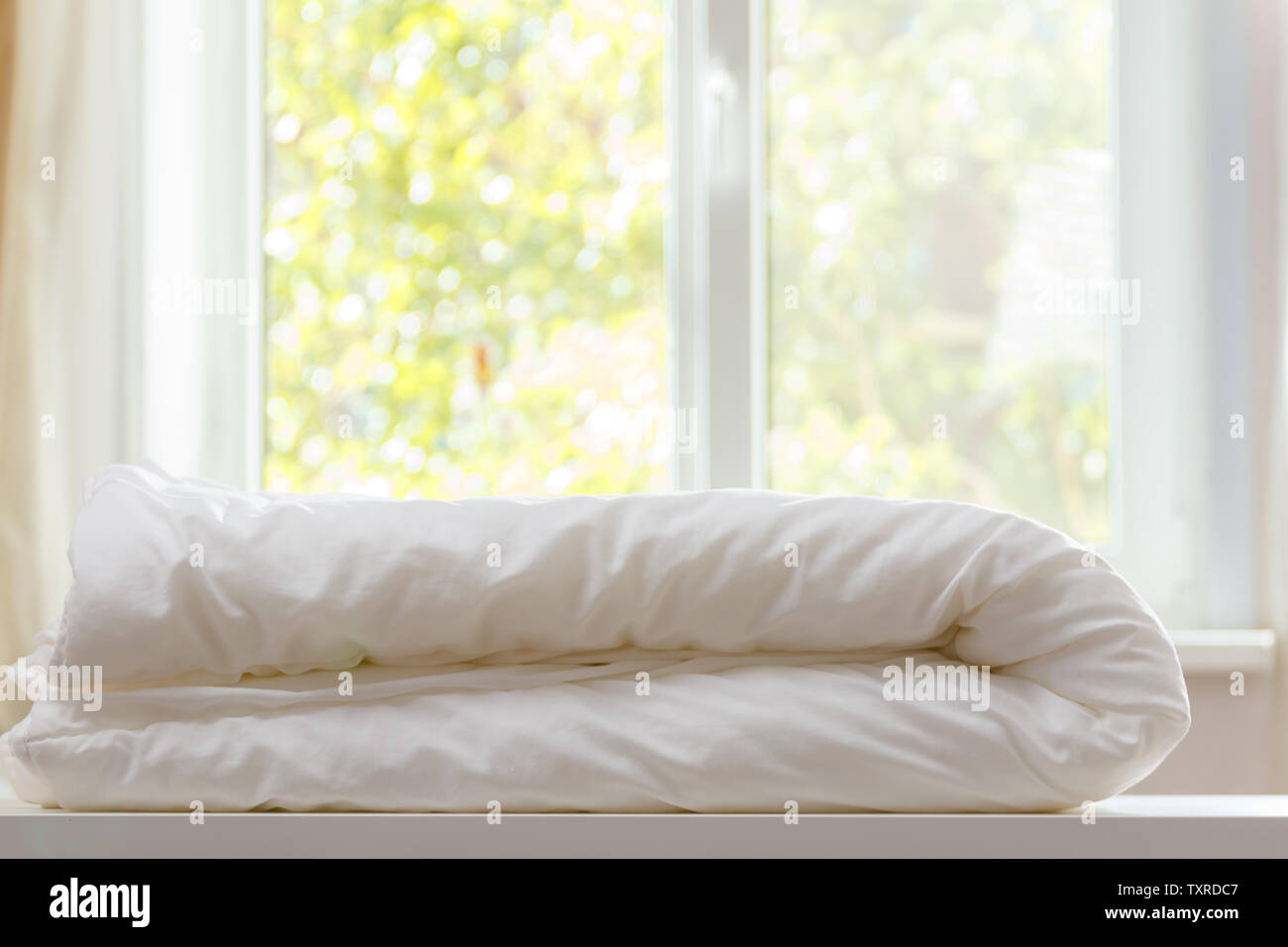 Un duvet blanc est posé sur la commode contre l'arrière-plan flou de la fenêtre. Banque D'Images