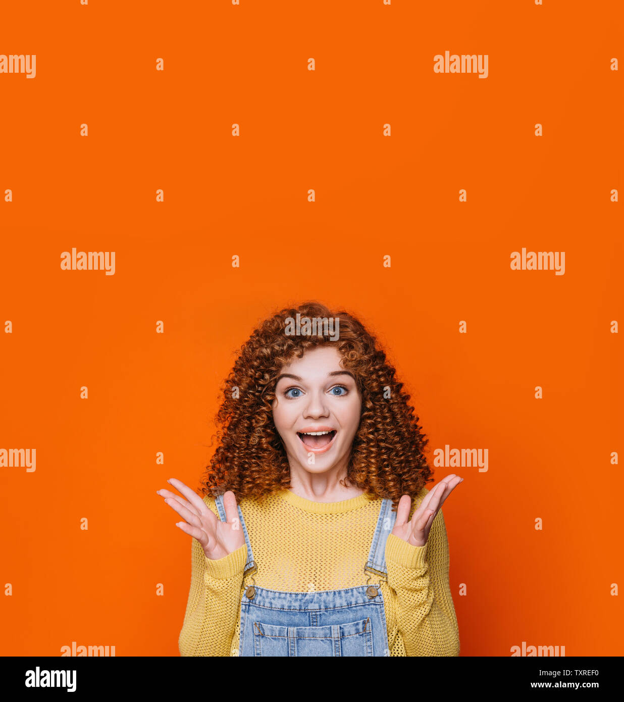 Curly red-haired woman faisant face choqué et soulevé les mains sur fond orange. Wow incroyable Banque D'Images