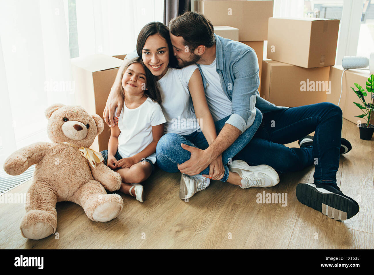 Happy Family hugging assis par terre dans leur nouvelle maison. C'est merveilleux de passer à un nouvel appartement Banque D'Images