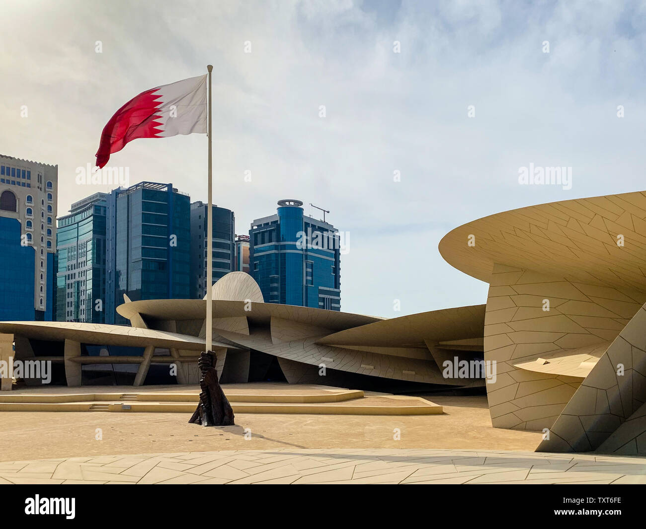 Musée national du Qatar, Doha. Le musée est en forme d'une rose du désert et est nouvellement construit. Skyline avec agitant le drapeau du Qatar. Banque D'Images