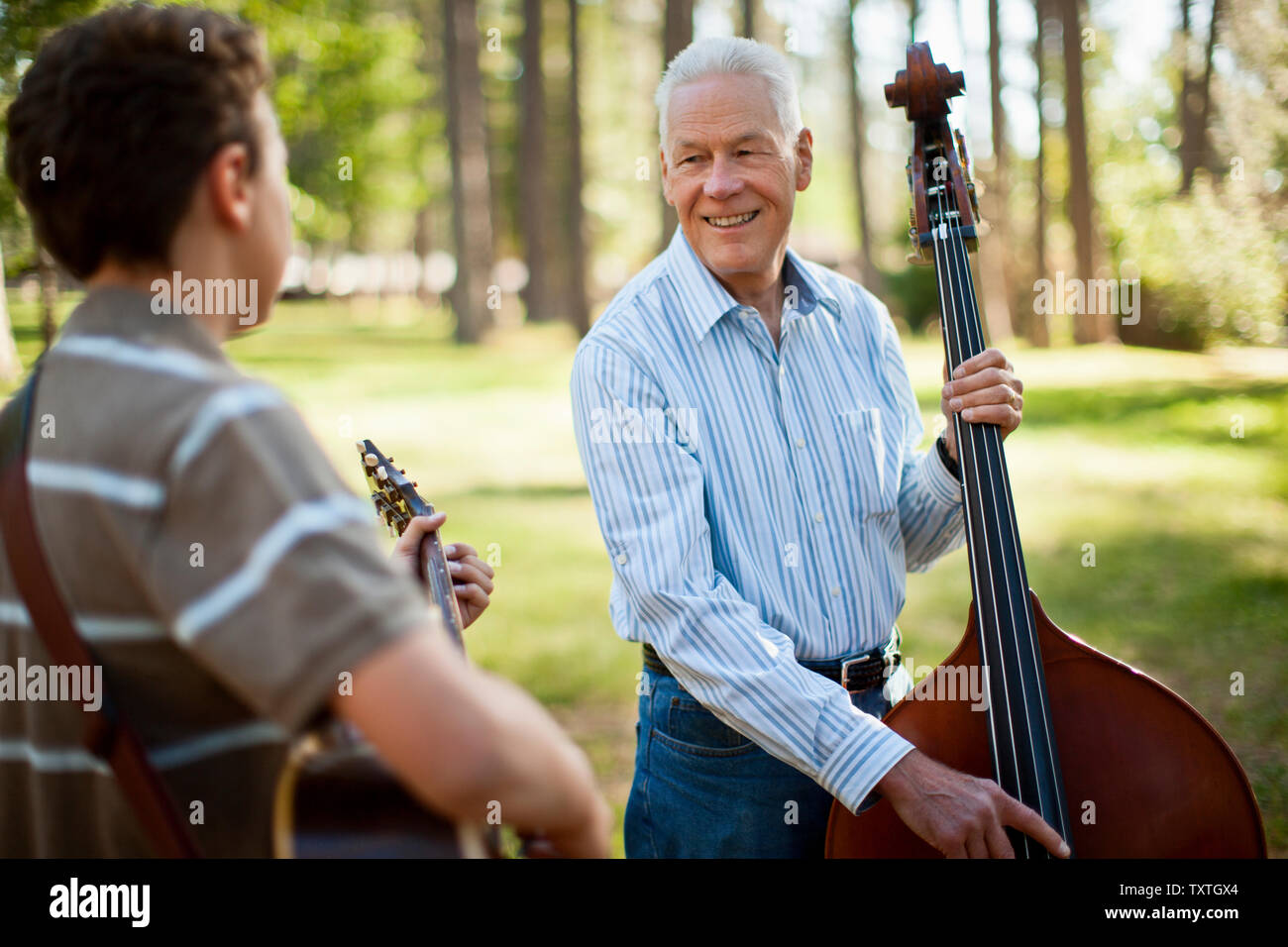 Smiling man une contrebasse alors que son petit-fils joue une guitare acoustique dans une forêt. Banque D'Images