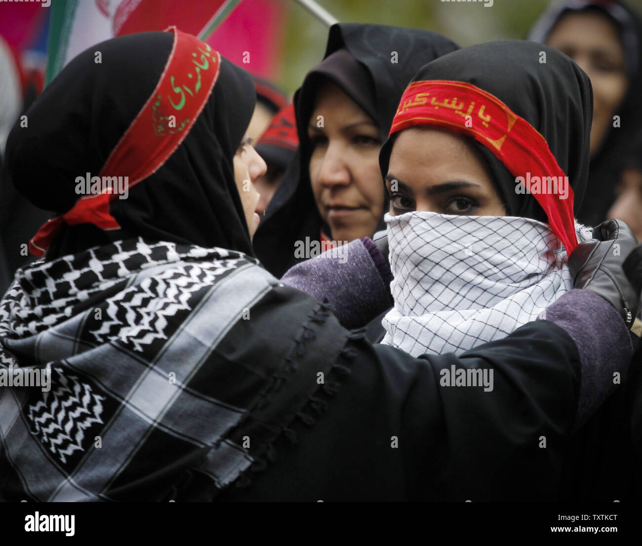 Membre de l'Iran's hardline bassidji aide un ami à couvrir son visage avec  foulard palestinien qu'ils assistent à un rassemblement marquant la semaine  Basij en face de l'ancienne ambassade américaine à Téhéran,
