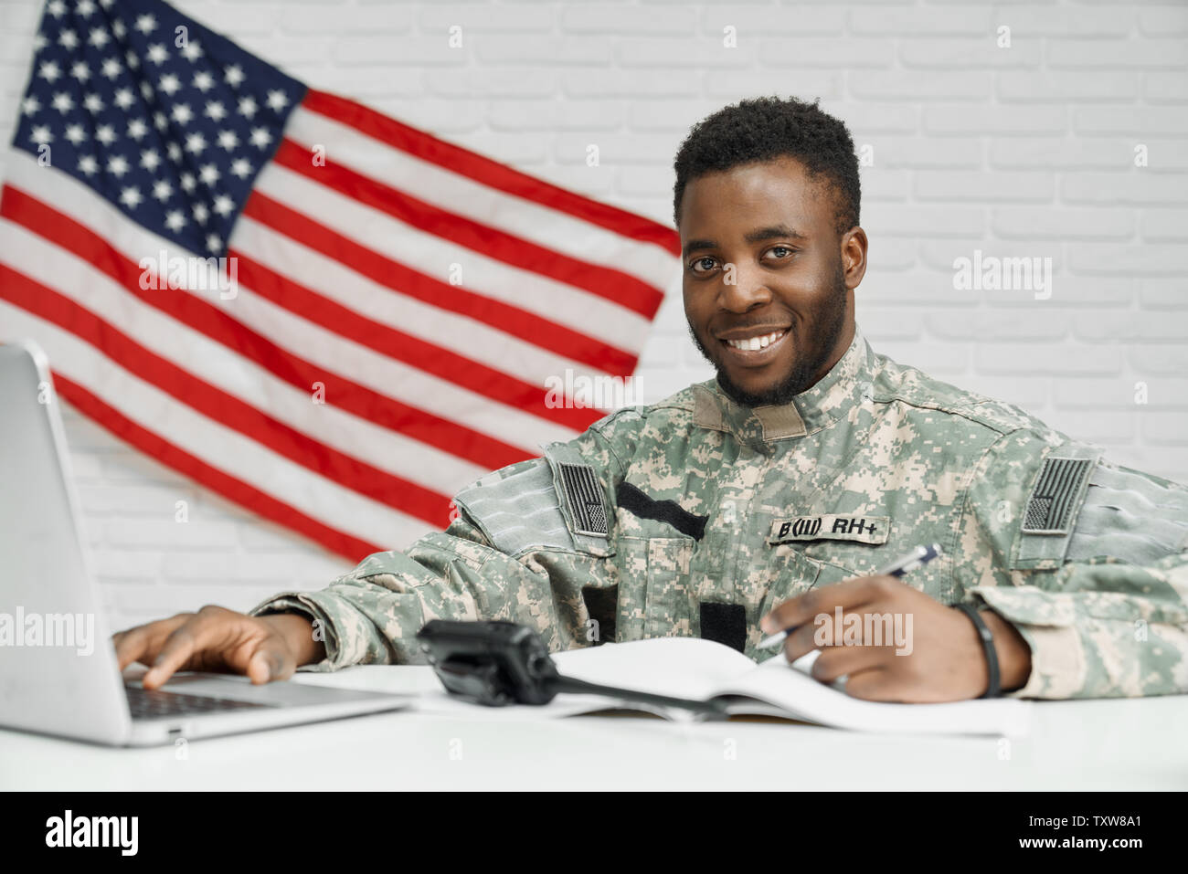 Soldat de positivité et travailleur de l'armée américaine, l'écriture de documents, using laptop and smiling at camera. Classement africain en uniforme l'abonnement contrat de service dans l'armée. Drapeau sur fond blanc. Banque D'Images