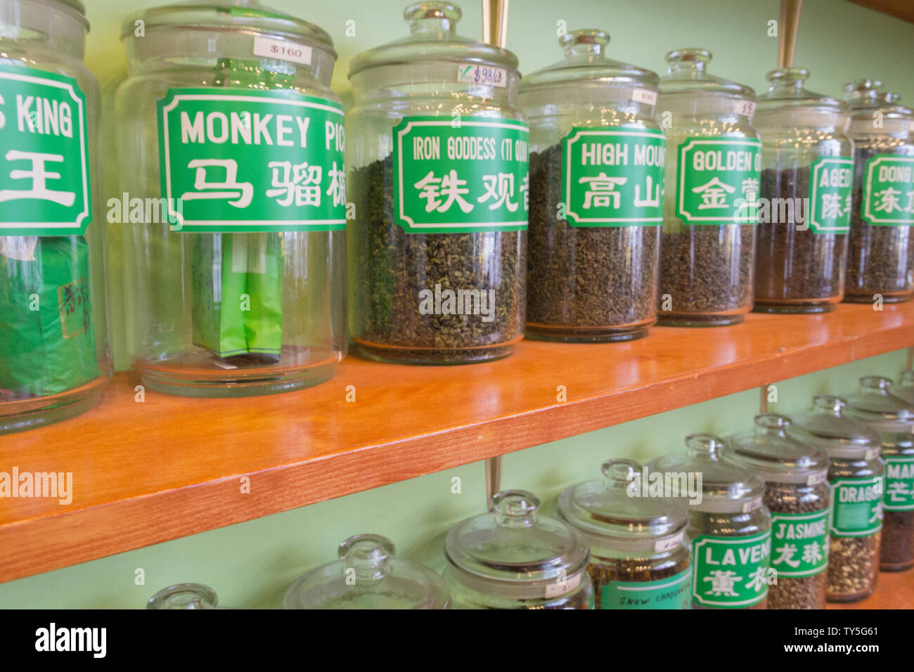 Une étagère pleine de thé médicinal traditionnel chinois dans de grands pots de verre avec une étiquette écrite en anglais et en chinois à la boutique de thé Chinois. Banque D'Images