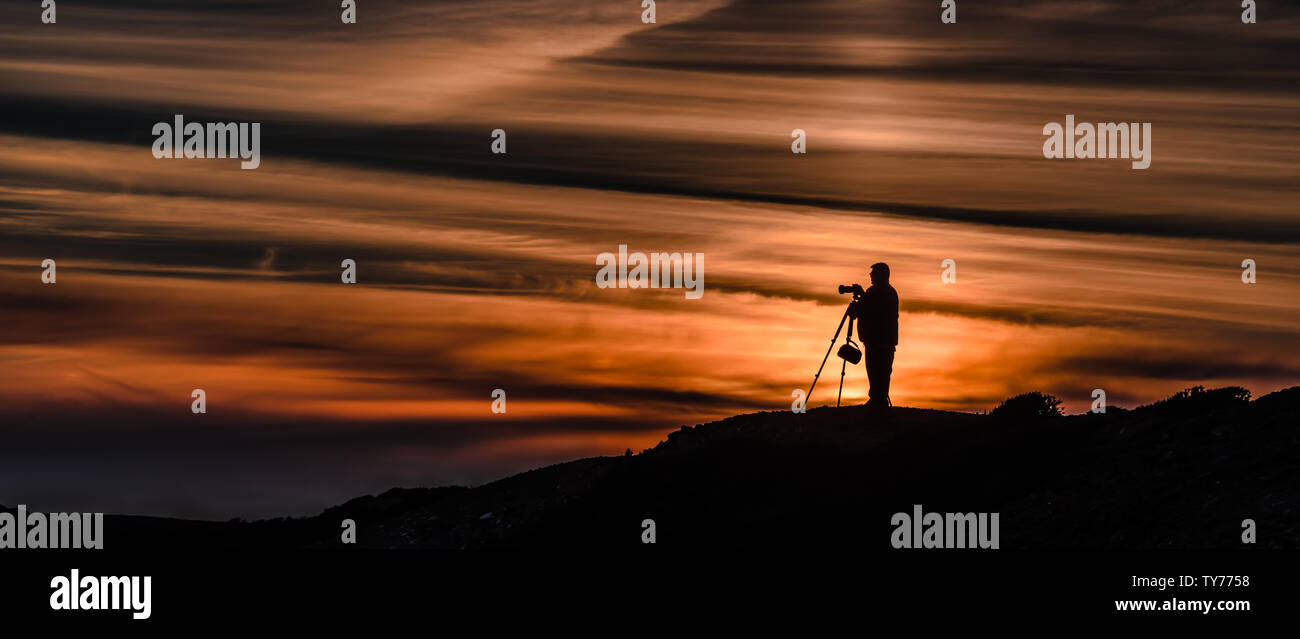 Une silhouette méconnaissable d'un photographe portrait au crépuscule avec trépied et appareil photo Banque D'Images