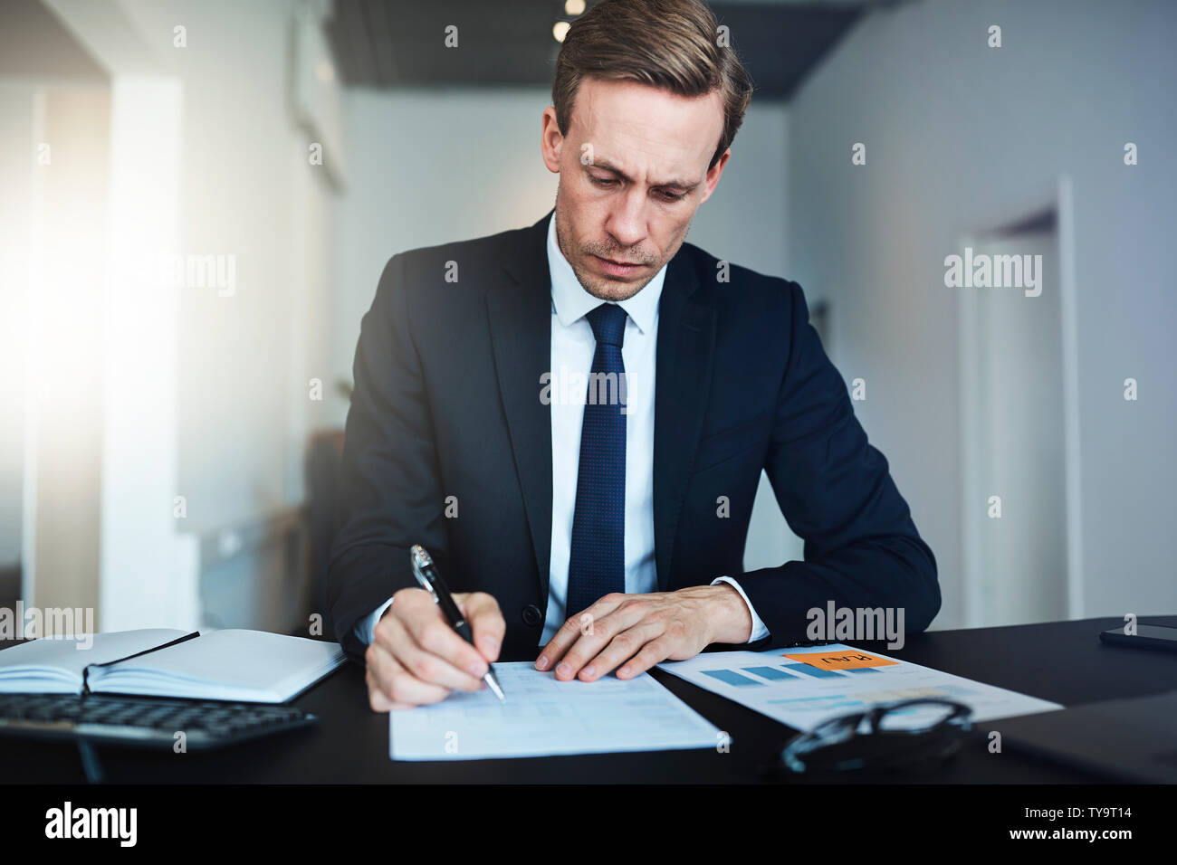 L'accent businessman reading les formalités administratives et de la signature de documents alors qu'il était assis à son bureau dans un bureau moderne et lumineux Banque D'Images