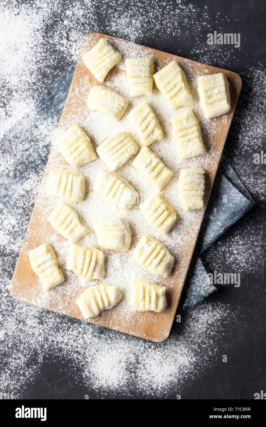 Gnocchi de pommes de terre maison crus brut avec de la farine sur une planche à découper. Vue d'en haut. Fond sombre. Banque D'Images