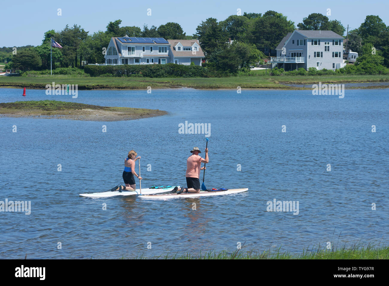 Un couple paddle boards passé, certaines maisons de luxe à Cape Cod, Massachsuetts, USA Banque D'Images