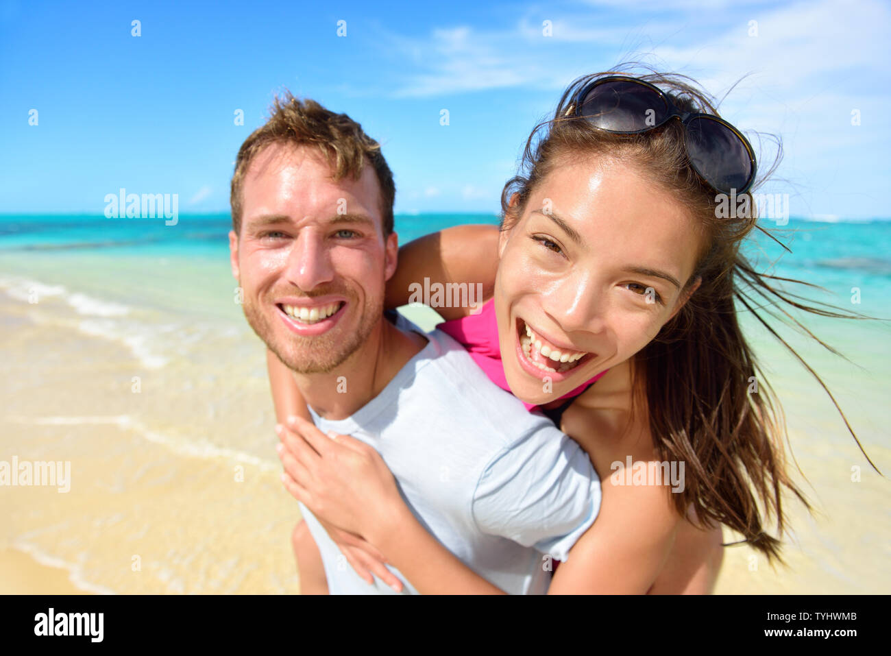 Jeune couple laughing on beach holidays. Belle asiatique mixed race woman greffant sur caucasien homme excité à portrait de l'appareil photo. Société multiculturelle, multiethnique, multiraciale. Banque D'Images
