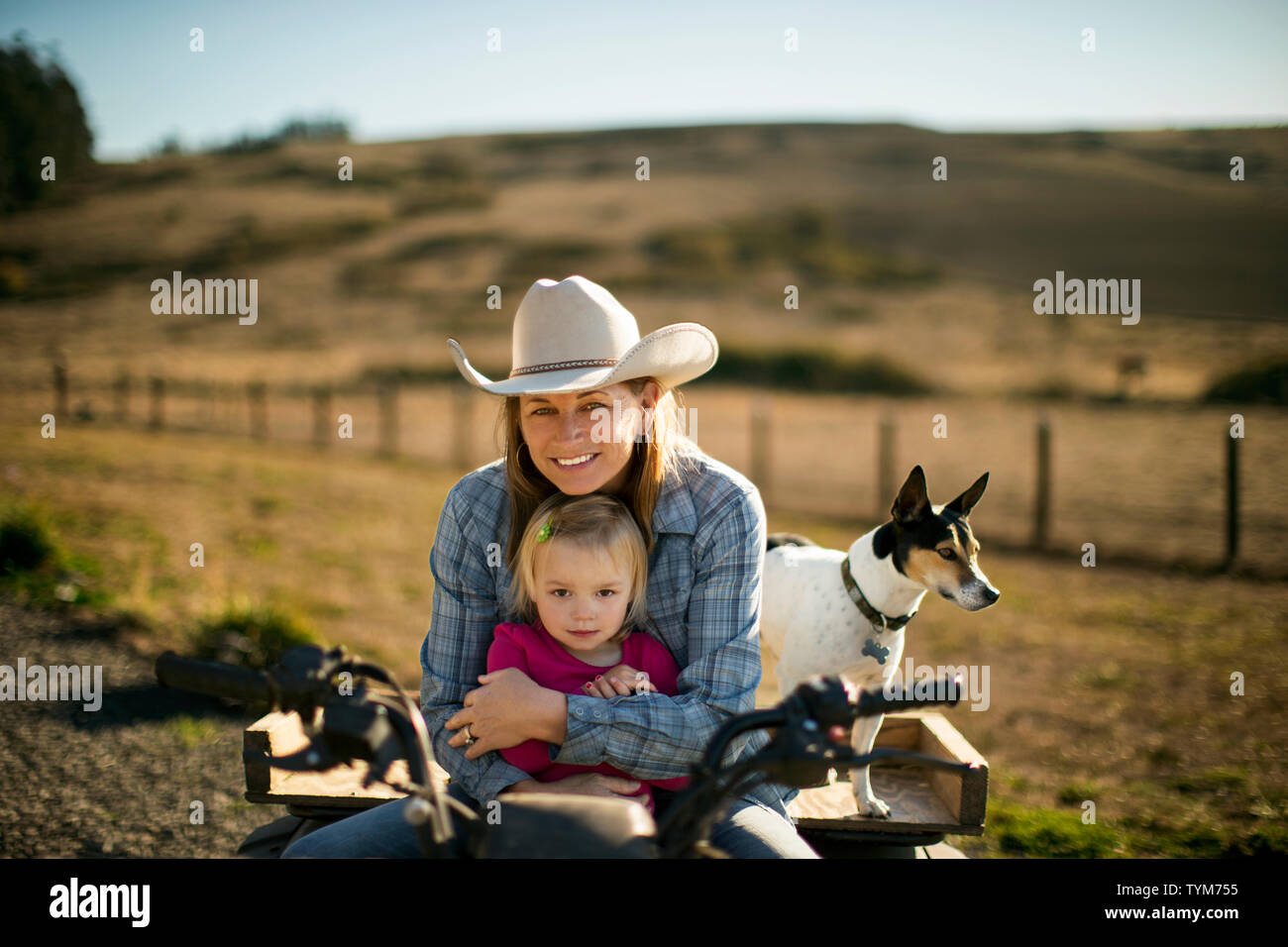 Portrait d'une femme de l'agriculteur et son tout-petit sur un quad pendant que leur chien se tient à côté d'eux. Banque D'Images