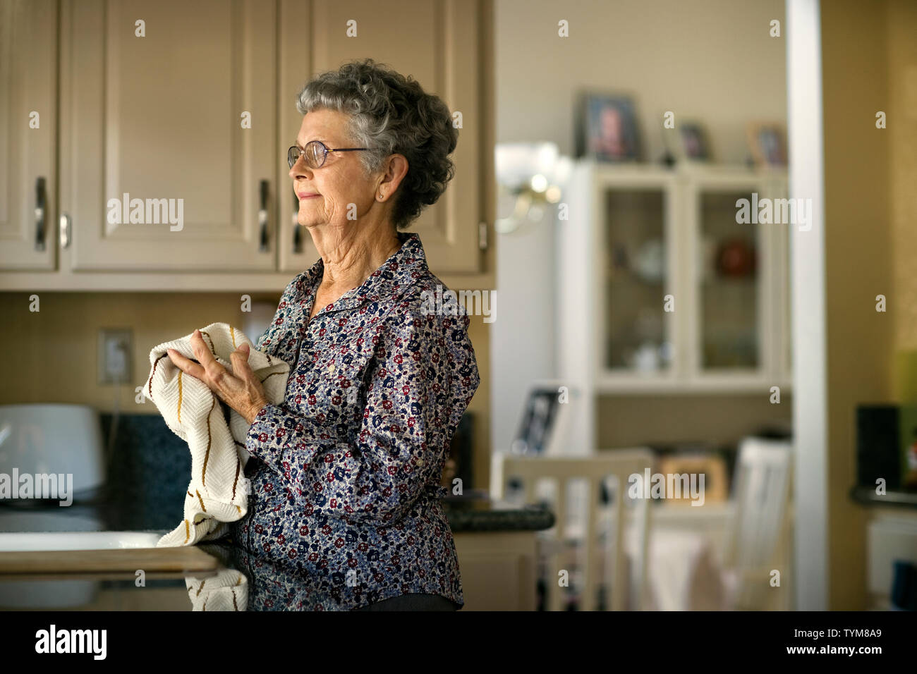 Femme âgée regarde pensivement hors de la fenêtre de la cuisine tout en faisant la vaisselle. Banque D'Images