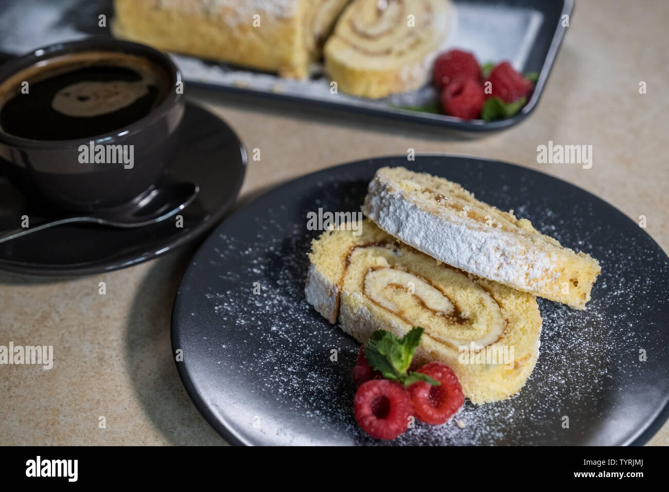 Swiss Roll avec de la confiture, décoré avec des framboises et de la menthe sur une assiette et café noir. Des bonbons. Focus sélectif. Banque D'Images