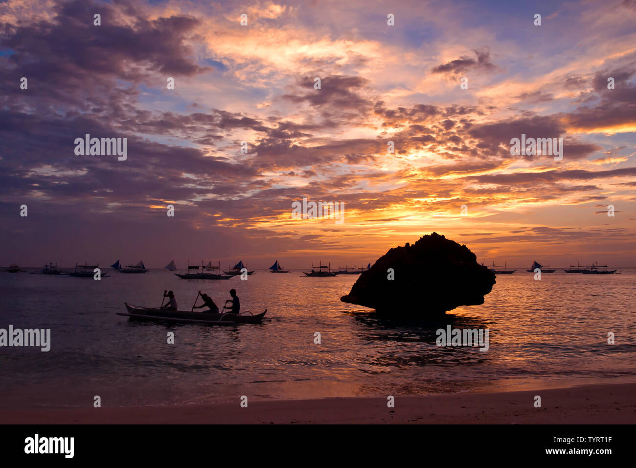 Trois hommes l'aviron d'un bateau de pêche au coucher du soleil près de white beach, Boracay Island, Philippines Banque D'Images