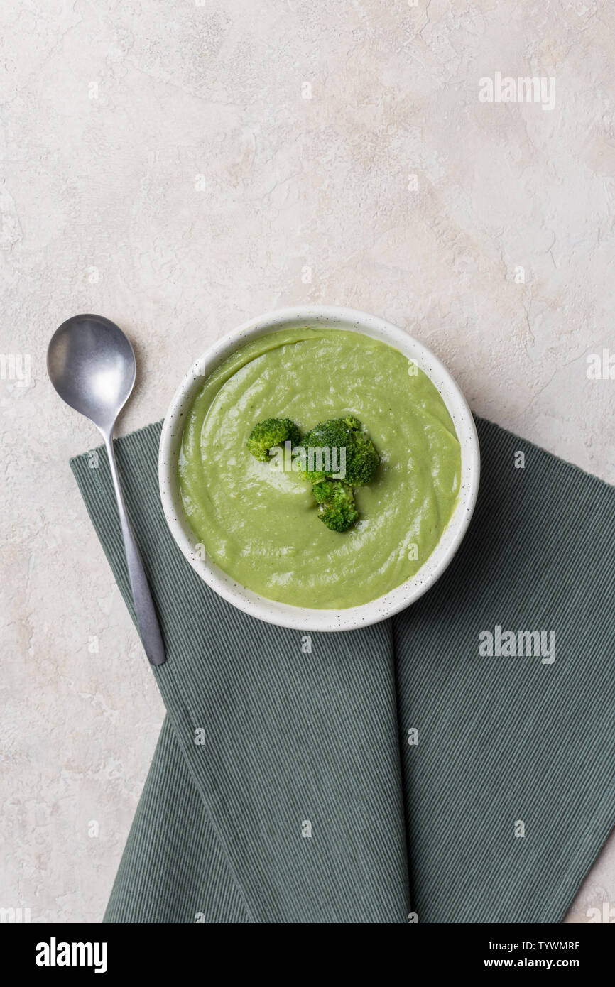 Soupe crème de brocoli frais dans un bol sur fond de béton léger avec serviette et cuillère. Concept de printemps de la nourriture. Vue d'en haut. Banque D'Images