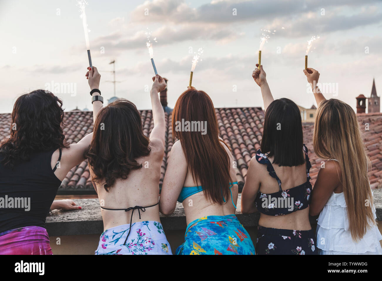 Groupe de professionnels amis féminins habillés en maillot de bain et paréo holding sparklers at rooftop party Banque D'Images