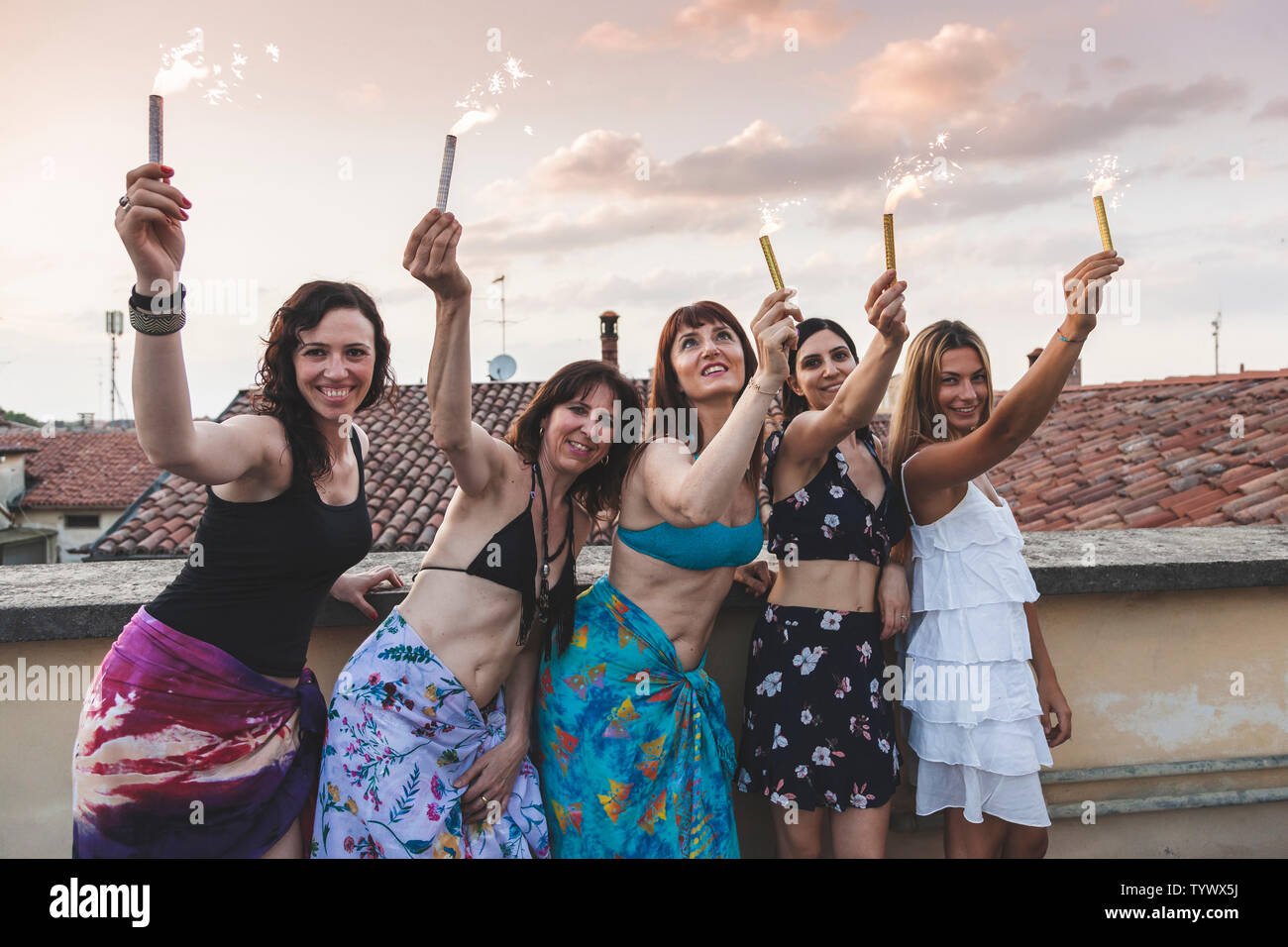 Groupe de professionnels amis féminins habillés en maillot de bain et paréo holding sparklers at rooftop party Banque D'Images