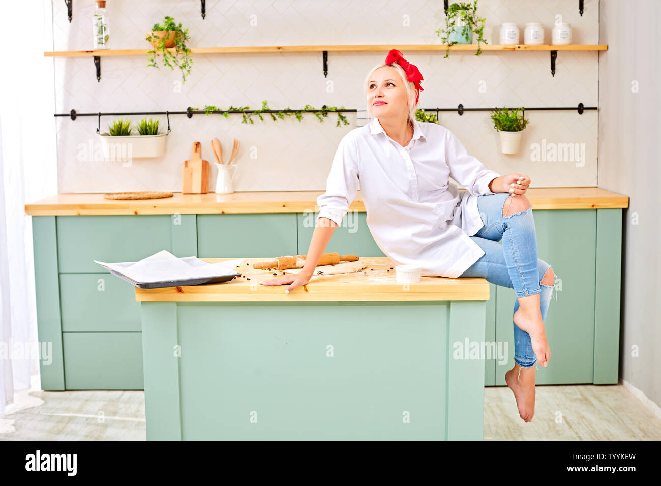 Jeune blonde avec un bandeau rouge dans une chemise blanche se trouve sur  la table de la cuisine avec de la pâte à cuire Photo Stock - Alamy