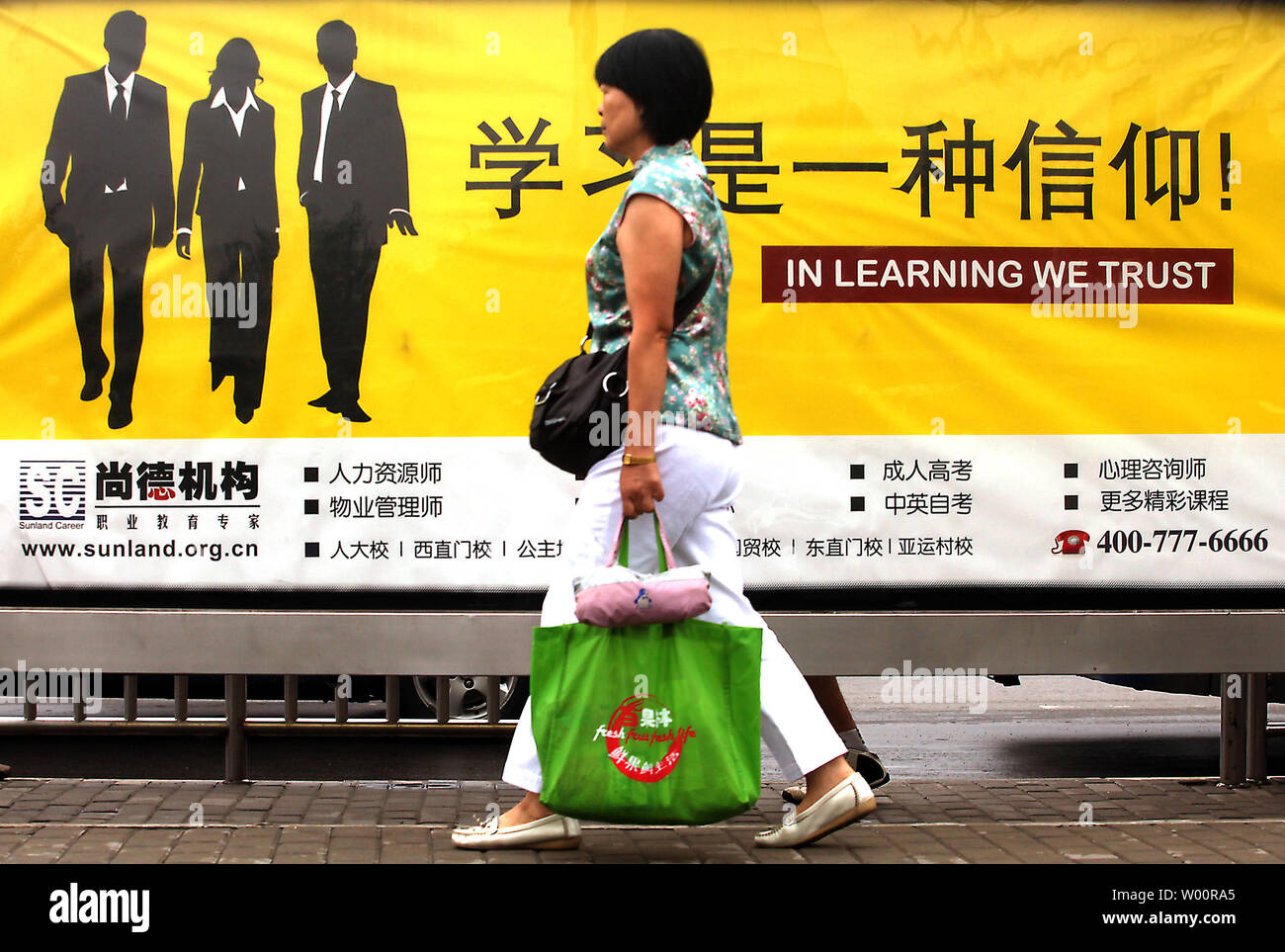 Une femme chinoise passe devant un arrêt de bus des panneaux publicitaires de cours particuliers en affaires et des compétences linguistiques à Pékin le 12 juillet 2010. Capitale de la Chine est devenue la dernière ville du continent désireux de renforcer les compétences en anglais de ses résidents dans le cadre des efforts déployés par le gouvernement pour être plus cosmopolite. Tous les employés du gouvernement en vertu de l'âge de 40 ans seront également tenus de maîtriser au moins 1 000 phrases en français de base pour leur travail quotidien. UPI/Stephen Shaver Banque D'Images