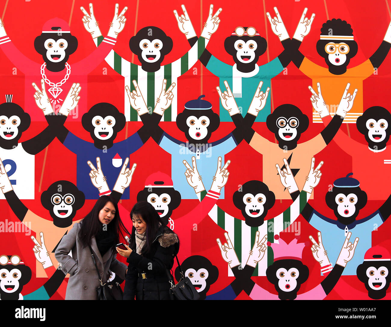 Femmes chinoises prendre vos autoportraits en face d'un mur décoré avec un montage de singes à Pékin le 25 février 2016. Cette année de neuf ans (année du singe) a été particulièrement faible, avec beaucoup moins d'artifice et des spectacles en plein air, en raison du ralentissement économique en Chine et de la pollution. Photo par Stephen Shaver/UPI Banque D'Images