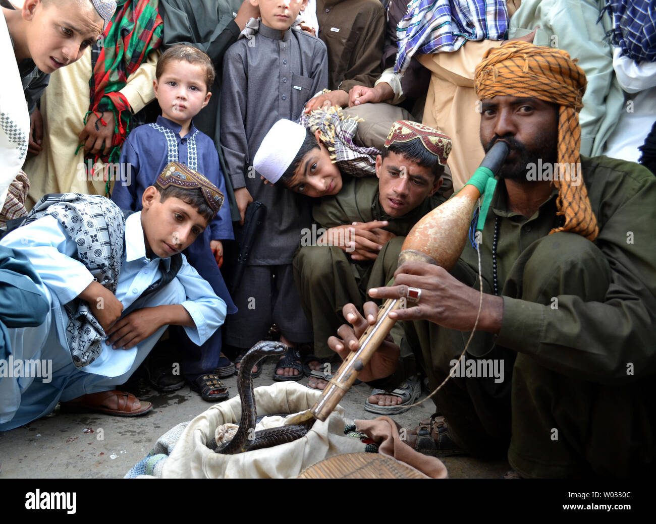 L'enfant regarde comme un charmeur de serpent joue le pungi pour faire le serpent 'dance' de la musique sur une route au Chaman, Pakistan, près de la frontière afghane le 9 août 2013. Les serpents ne peuvent pas entendre la musique, mais ils ne le son sens et donc augmenter à partir du panier. UPI/Matiullah Banque D'Images