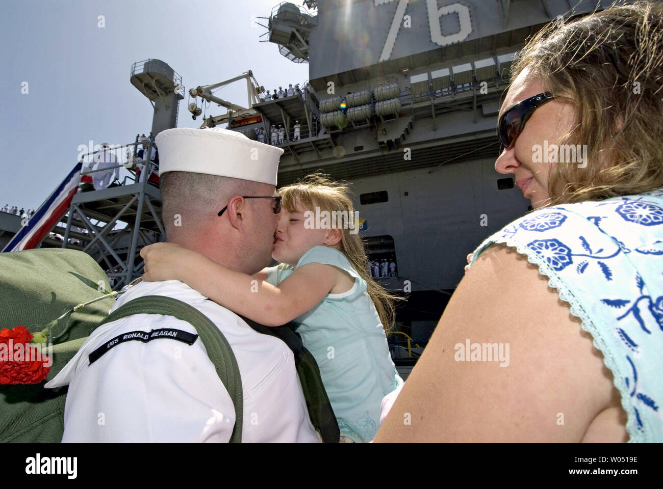 Richard marin Depalma obtient un baiser à partir de 4 ans fille Chloe comme son épouse Joy regarde sur son navire après le porte-avions USS Ronald Reagan est arrivé, le 6 juillet 2006, à la Naval Air Station North Island à Coronado, en Californie. . Le porte-avions à propulsion nucléaire et de son équipage de près de 5 000 marins est retourné à San Diego après un déploiement de six mois dans le golfe Persique et l'océan Pacifique occidental. C'était la première mission pour le navire depuis sa mise en service en 2003. (Photo d'UPI / Earl S. Cryer) Banque D'Images