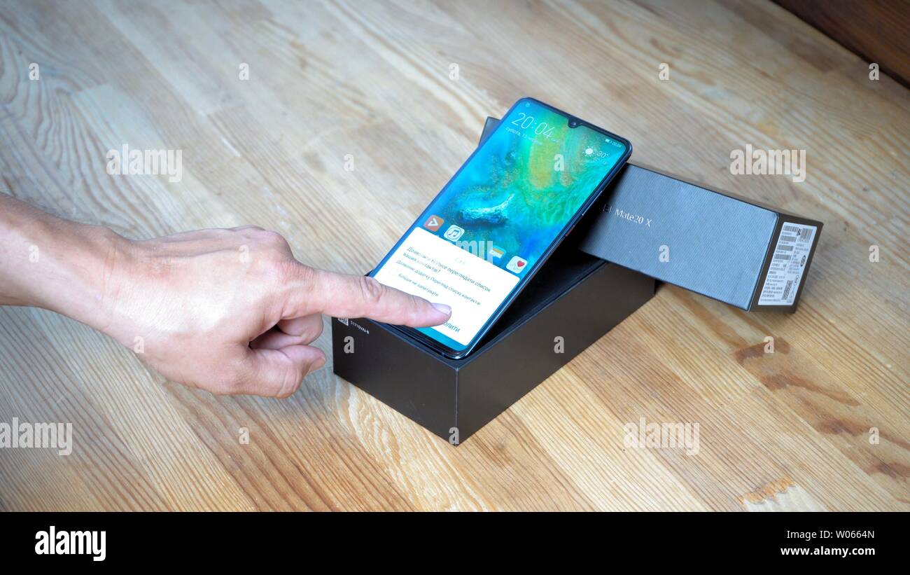 Téléphone avec l'écran allumé se trouve dans la case sur la table en bois. L'homme est cliquant sur smartphone Huawei Mate 20 x affichage pour montrer ses possibilités de réglages Banque D'Images