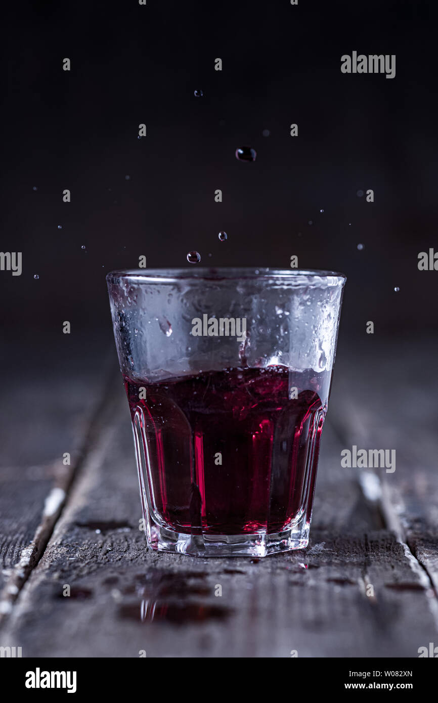 Shot de liqueur amère rouge avec des gouttes éclaboussant sur bois Banque D'Images