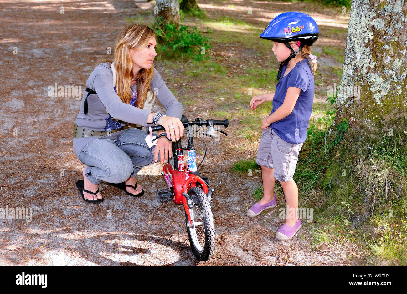 Une mère, d'une trentaine d'années maintenant le vélo de sa fille de quatre ans dans la forêt Banque D'Images