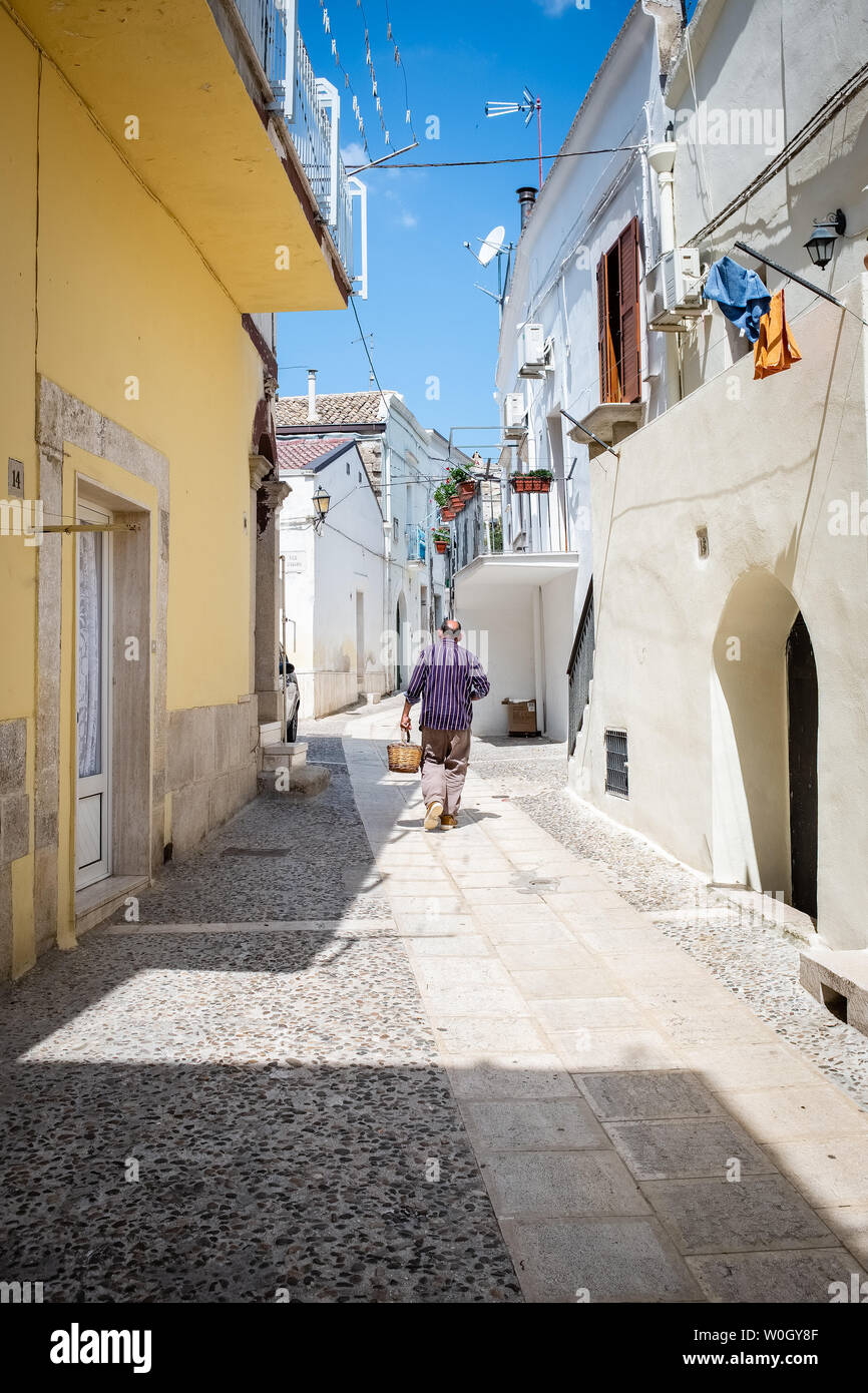 SPINAZZOLA, ITALIE - 21 août 2018 : vieil homme marche dans une rue pavée en pierre portant un panier de paille Banque D'Images