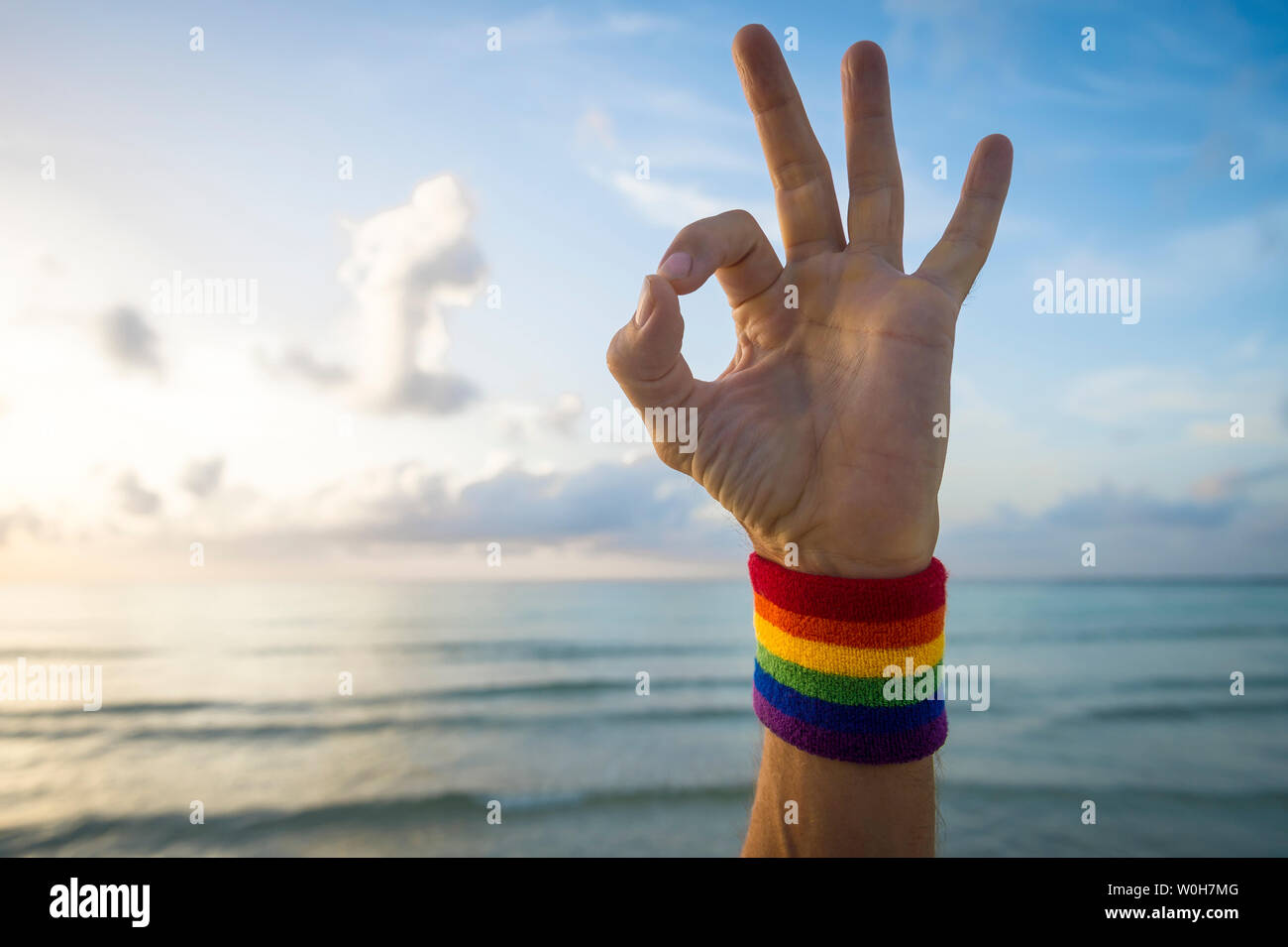 De la main donnant l'athlète signe OK avec gay pride couleurs arc-en-ciel contre bracelet soft horizon sur mer tropical calme à la plage Banque D'Images