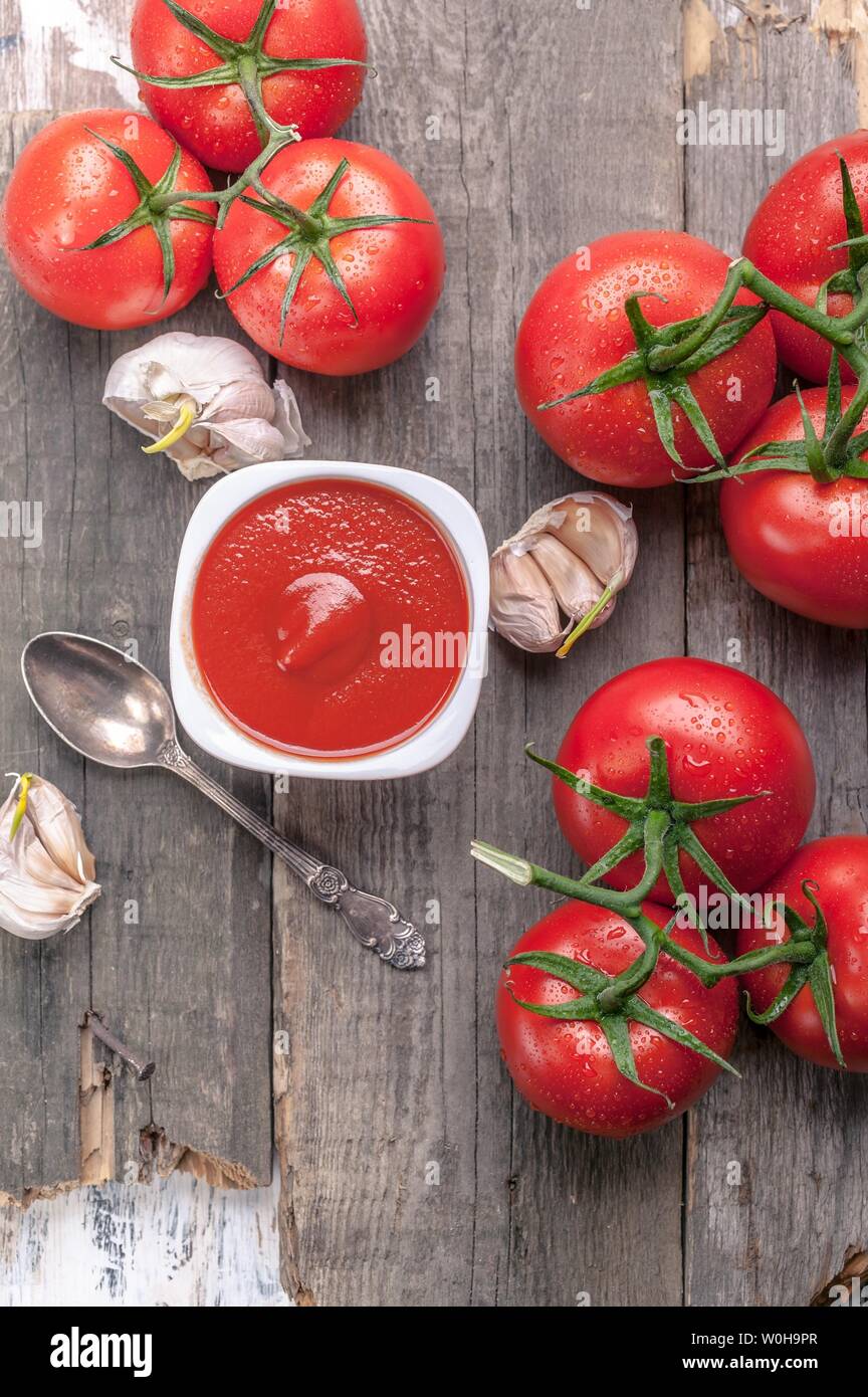 Vue de dessus du ketchup ou de la sauce tomate, l'ail et tomates fraîches sur une branche sur un fond rustique. Shot verticale Banque D'Images