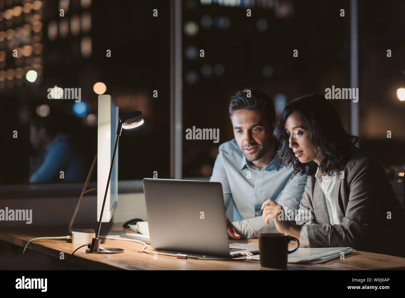 Deux jeunes gens d'affaires travaillant en heures supplémentaires ensemble au cours d'un ordinateur portable à un bureau bureau tard dans la soirée Banque D'Images