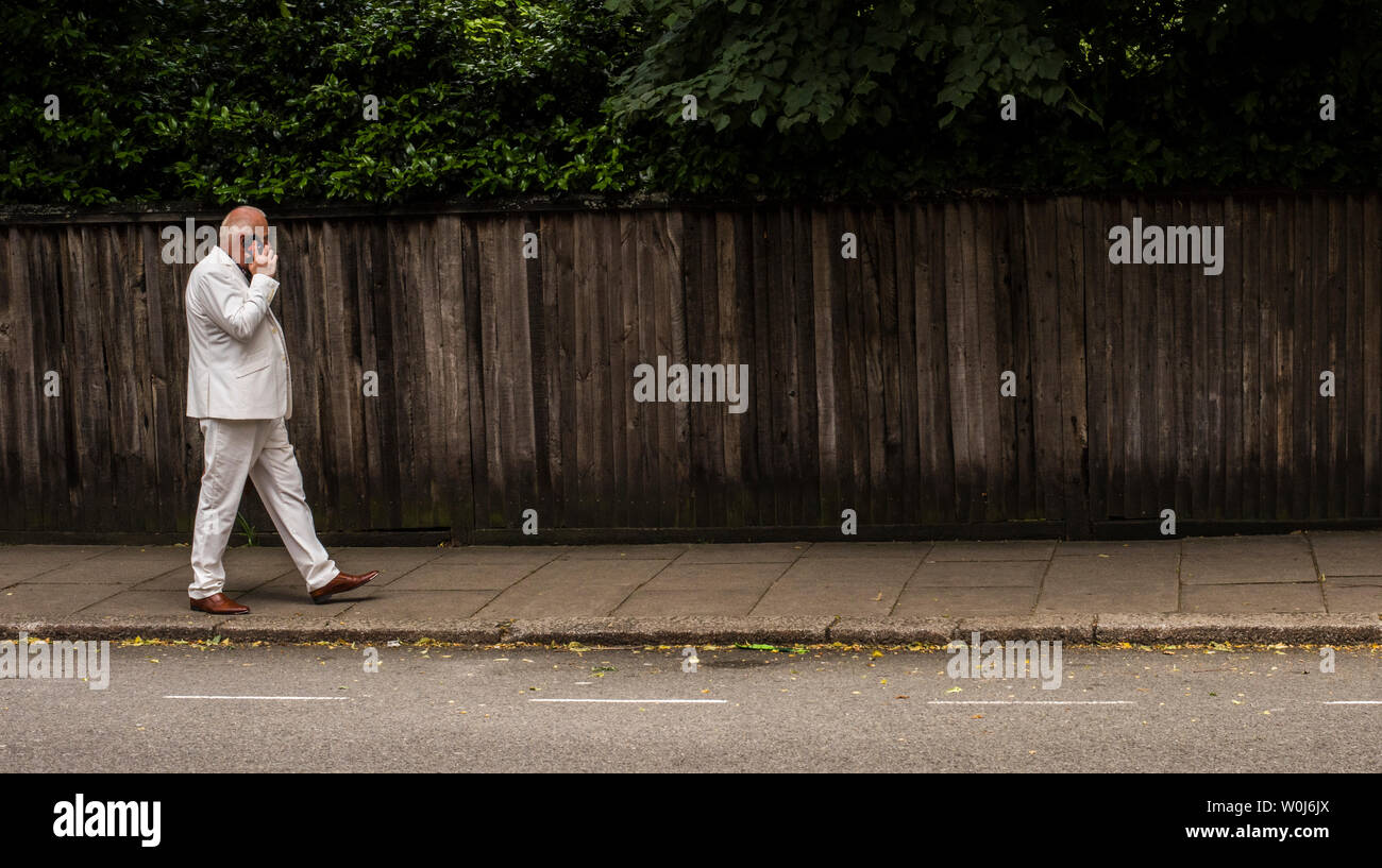 Homme portant un costume blanc à l'aide de téléphone mobile sur la chaussée, London, England, UK Banque D'Images