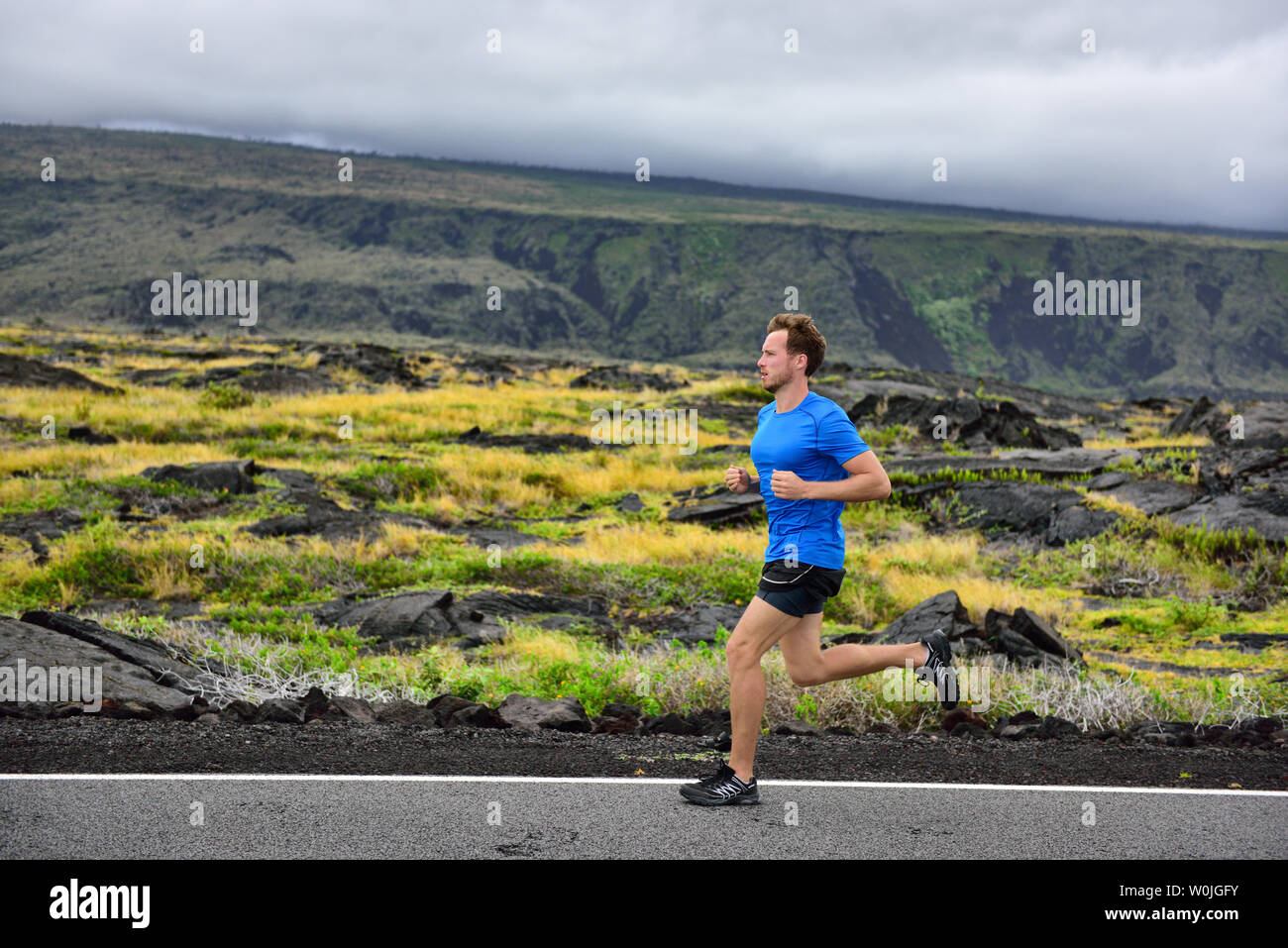 Homme sportif runner s'exécutant sur route de montagne. Running Man jogging cardio formation rapide pour le marathon sur chemin de campagne dans la nature, paysage d'arrière-plan le volcan. Les jeunes adultes de race blanche dans son 20s. Banque D'Images
