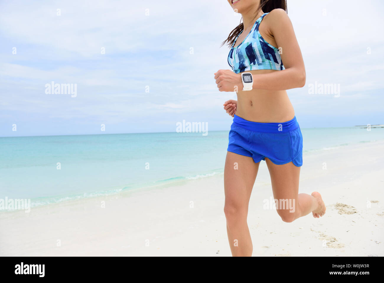Runner exécutant portant des smartwatch. Remise en forme de femme portant  un short bleu et de soutien-gorge de sport cardio training sur beach en  utilisant app sur smart watch pour surveiller la